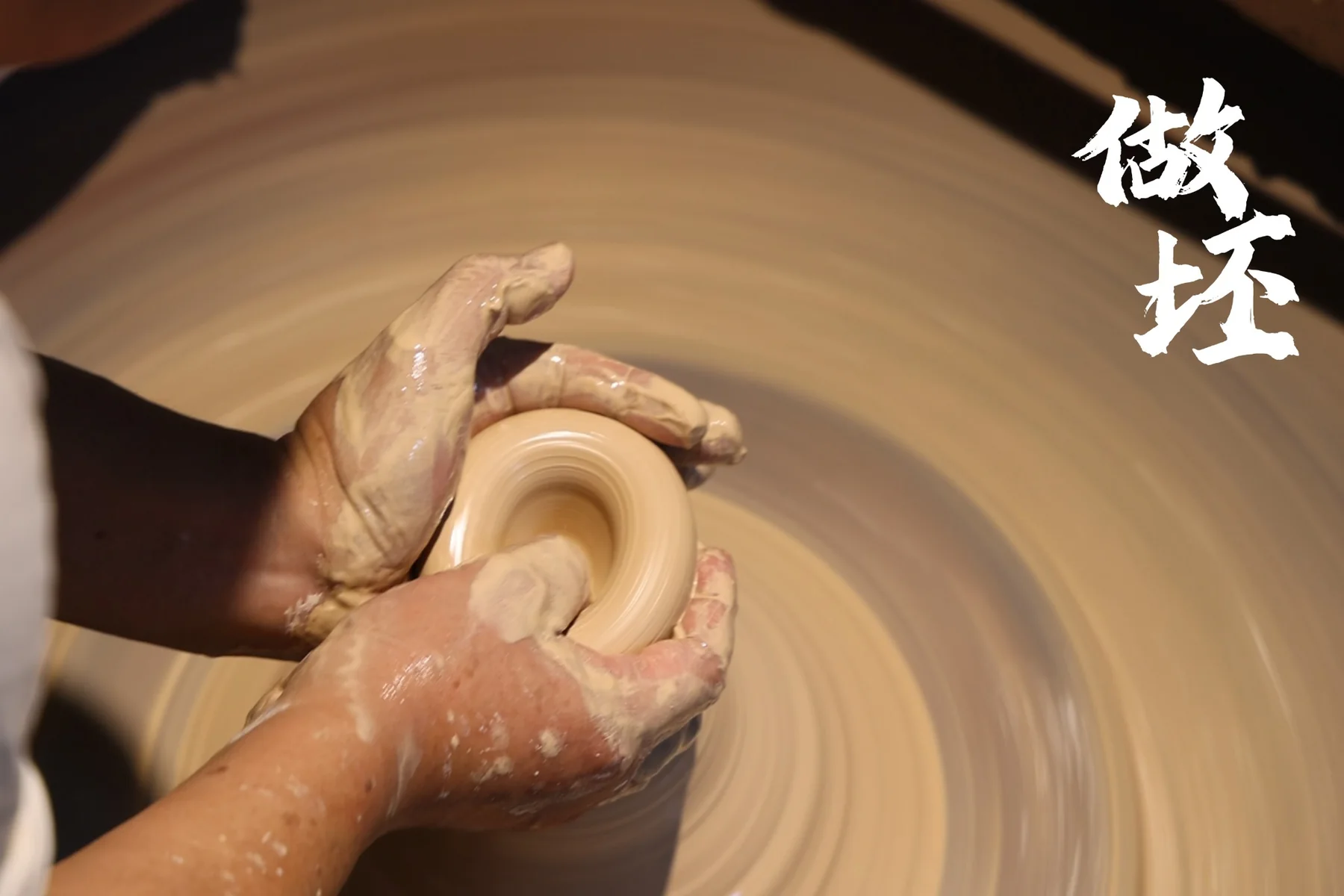 Hands forming porcelain on a spinning wheel